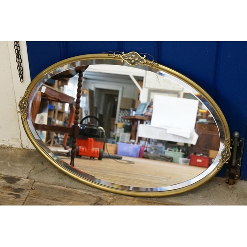 606 - An Oval Art Nouveau designed Brass Framed Mirror with a bevelled edge. Measuring: 69cms x 42cms.