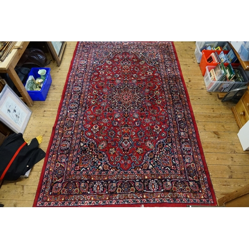 530 - A large red ground rug, with fringe decoration. Measuring 330cm x 202cm.