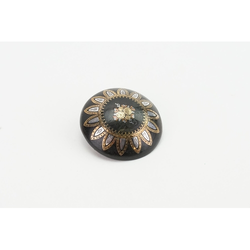 250 - A tortoise shell pique brooch, with inlaid decoration. Gold and silver coloured design.