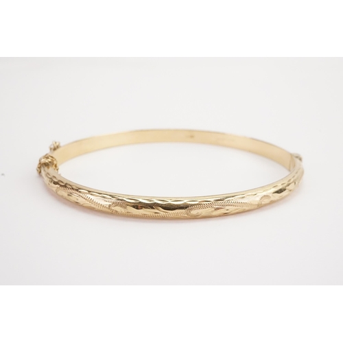 140 - A 9ct gold engraved bangle, with safety chain. Weight 6.4g.