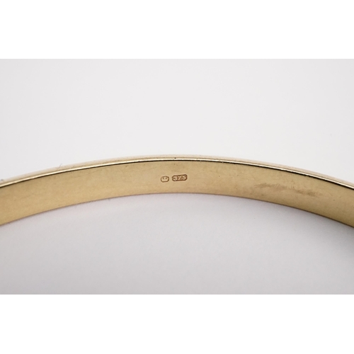 140 - A 9ct gold engraved bangle, with safety chain. Weight 6.4g.