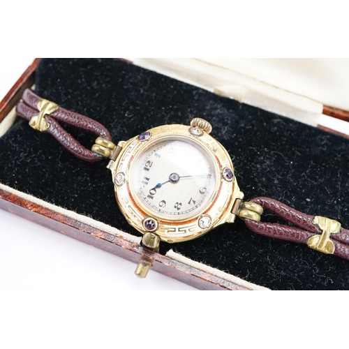 180 - A 18ct gold diamond and amethyst set wrist watch, Greek key white and red enamel design, brown leath... 