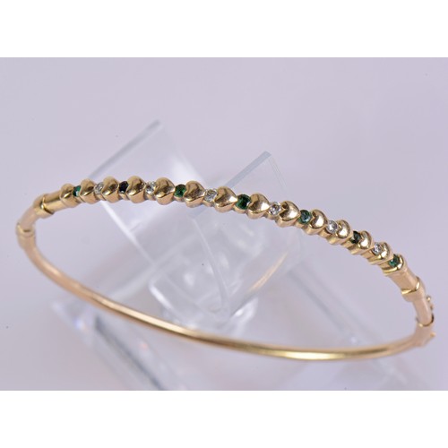 39 - A 9ct gold bangle designed with heart motifs, set with six diamonds and seven emeralds, and fitted w... 