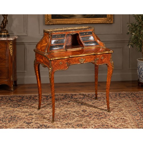 A Late 19th Century Amarinth & Purple Heart inlaid Ladies Writing Desk fitted with a bank of Six Leather & Gilt Fronted Drawers, Clock Housing interior, Bombe Sides, Gilt Metal Mounted & Surround, Three Graduated Drawers, Slender Shaped Feet & Sabots. Measuring: 70cms across x 44cms deep x 92cms high. Label Underneath Marked: 85/ST/L/ULT.