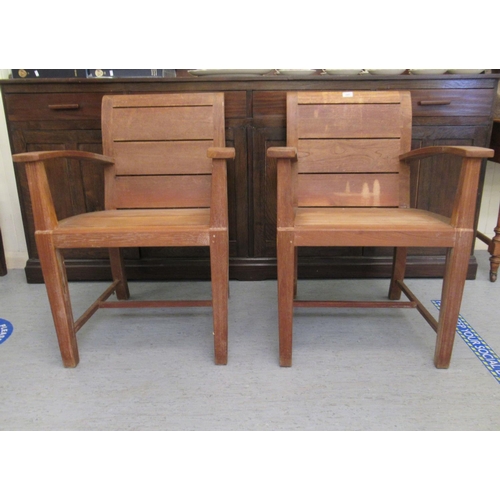 345 - A pair of modern teak patio chairs, each with a solid backs and seats, raised on block legs