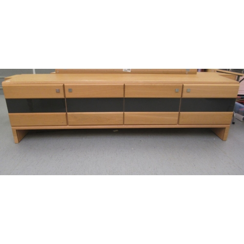 64 - A modern Casino light oak sideboard, comprising four inline doors with smoked glass panels, raised o... 