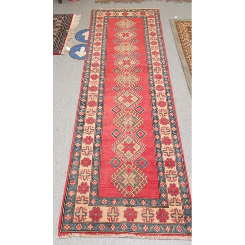 188 - An Afghan Kazak runner, decorated with repeating central diamond shaped motifs, on a multi-coloured ... 