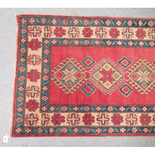 188 - An Afghan Kazak runner, decorated with repeating central diamond shaped motifs, on a multi-coloured ... 