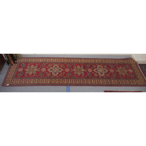 189 - An Afghan Kazak runner, decorated with repeating central stylised decoration, on a red and multi-col... 