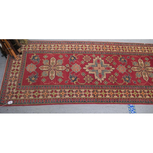 189 - An Afghan Kazak runner, decorated with repeating central stylised decoration, on a red and multi-col... 