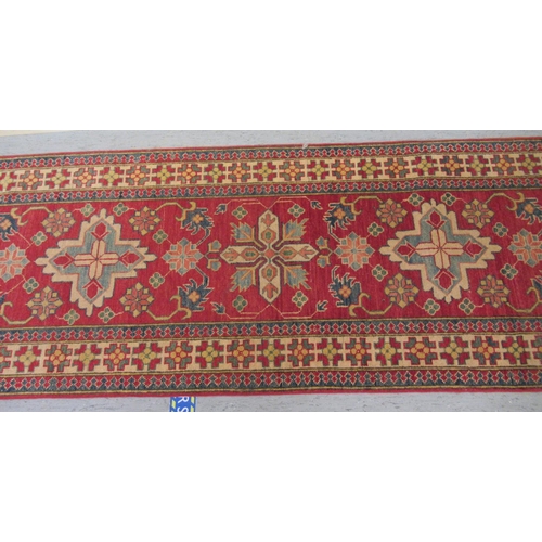 189 - An Afghan Kazak runner, decorated with repeating central stylised decoration, on a red and multi-col... 