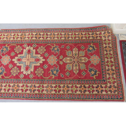 189 - An Afghan Kazak runner, decorated with repeating central stylised decoration, on a red and multi-col... 