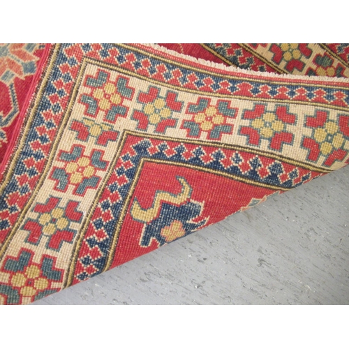 189 - An Afghan Kazak runner, decorated with repeating central stylised decoration, on a red and multi-col... 