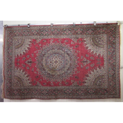 180 - A Persian rug, decorated with a central starburst design medallion, bordered by floral designs, on a... 