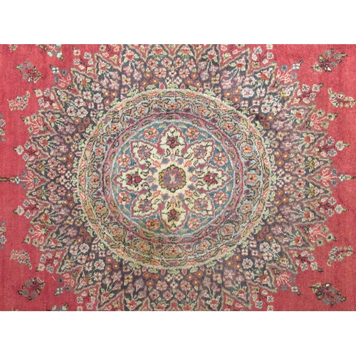 180 - A Persian rug, decorated with a central starburst design medallion, bordered by floral designs, on a... 