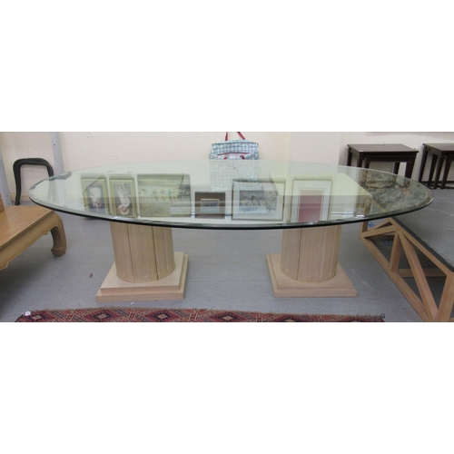 118 - A modern glass top dining table of oval form, raised on two cream coloured painted pillar design ped... 