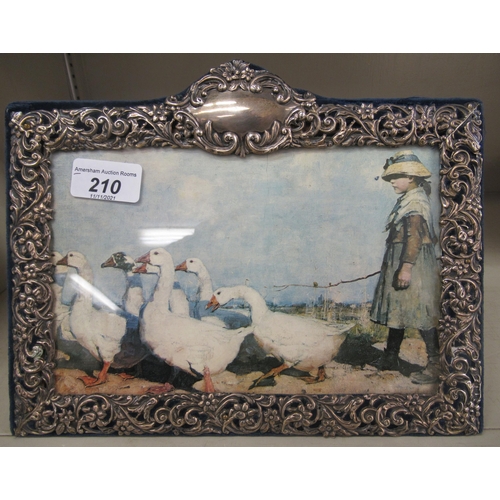 210 - An Edwardian silver picture frame on a fabric back, decorated with flora, scrolls and a vacant carto... 