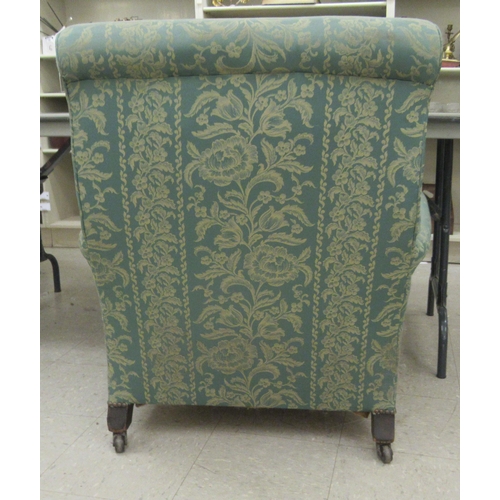 226 - An early 20thC armchair, having a high, scrolled back, upholstered in floral patterned green fabric ... 