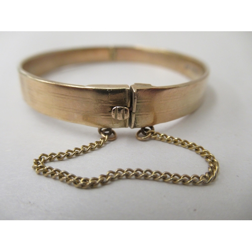 241 - A 9ct gold hinged bangle, on a safety chain 