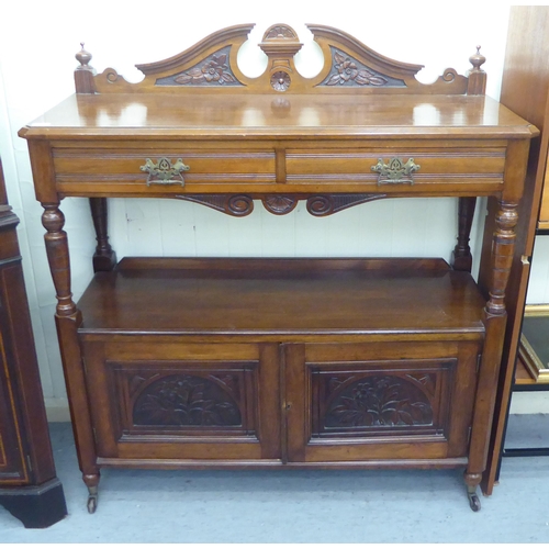 104 - A late Victorian mahogany carved buffet with two inline drawers, over an open shelf and two door cup... 