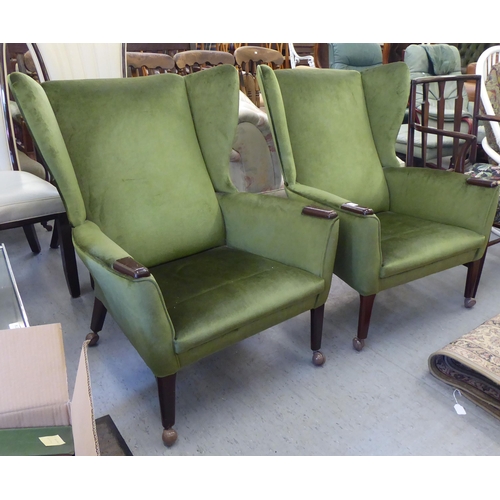 134 - A pair of (possibly) Parker Knoll green fabric upholstered enclosed wingback armchairs, raised on ta... 