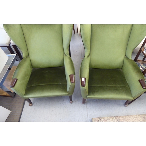 134 - A pair of (possibly) Parker Knoll green fabric upholstered enclosed wingback armchairs, raised on ta... 