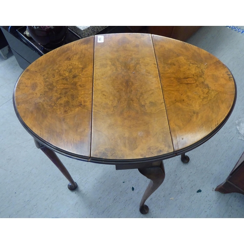 184 - A 1920s walnut gateleg side table, the oval, quarter veneered top with D-shaped fall flaps, raised o... 