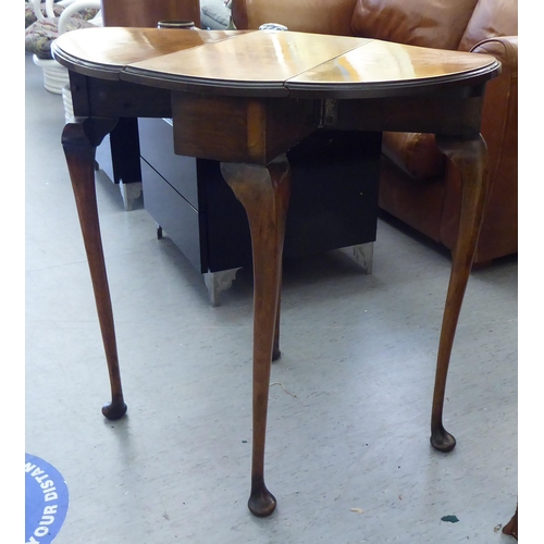 184 - A 1920s walnut gateleg side table, the oval, quarter veneered top with D-shaped fall flaps, raised o... 