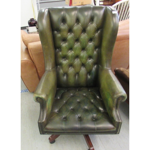 215 - A modern Georgian inspired high wingback chair, button upholstered in studded olive green hide, rota... 