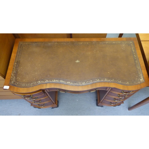 257 - A Reprodux yewwood veneered serpentine front, nine drawer twin pedestal desk with brass bail handles... 