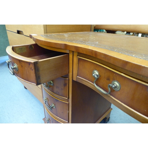 257 - A Reprodux yewwood veneered serpentine front, nine drawer twin pedestal desk with brass bail handles... 