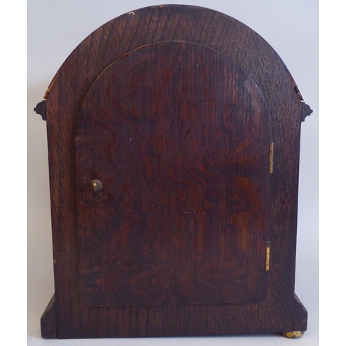 61 - An early 20thC round arch, oak cased bracket clock; the gong strike movement faced by a silvered and... 