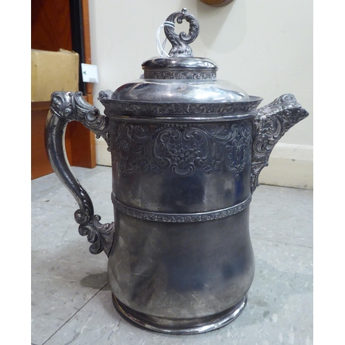 181 - An early/mid 20thC American quadruple plated, lidded jug, decorated with C-scrolled and foliate deco... 