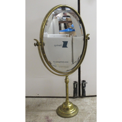 194 - An early 20thC brass framed dressing room toilet mirror, the bevelled plate pivoting/rotating on a t... 