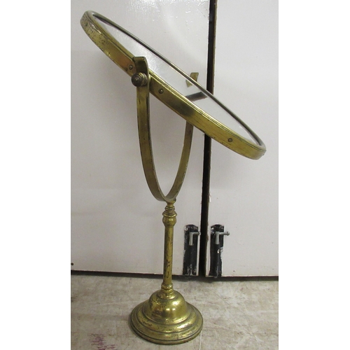 194 - An early 20thC brass framed dressing room toilet mirror, the bevelled plate pivoting/rotating on a t... 