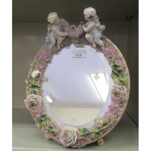 222 - A late 19thC (probably German) oval dressing table mirror, the bevelled plate set in a floral encrus... 