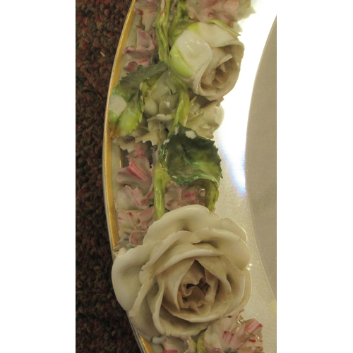 222 - A late 19thC (probably German) oval dressing table mirror, the bevelled plate set in a floral encrus... 