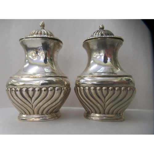 57 - A three piece silver condiments set of oval demi-reeded form  comprising two pepper pots; and a... 