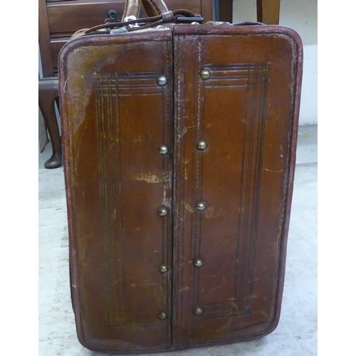 11 - An early 20thC moulded and stitched mid brown hide suitcase with brass studs, a lockable catch and a... 