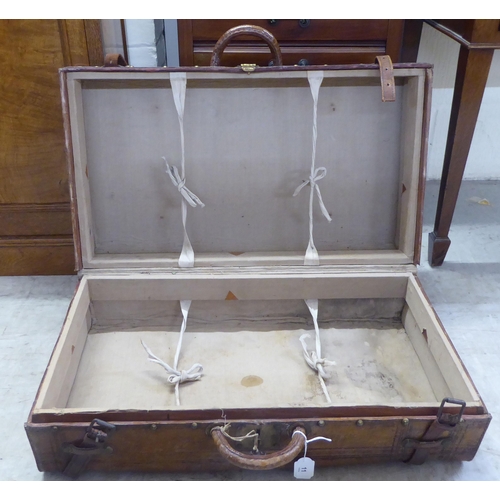 11 - An early 20thC moulded and stitched mid brown hide suitcase with brass studs, a lockable catch and a... 