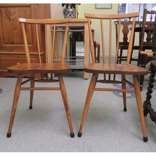 13 - Two Ercol beech and elm framed chairs with curved bar backs and spindle supports, the solid seats ra... 