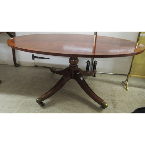 138 - A reproduction mahogany finished oval coffee table, raised on splayed legs with brass capped casters... 