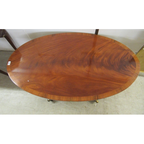 138 - A reproduction mahogany finished oval coffee table, raised on splayed legs with brass capped casters... 