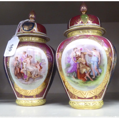 169 - A pair of early 20thC Vienna porcelain vases and covers, decorated with gilded cartouches, on a mult... 