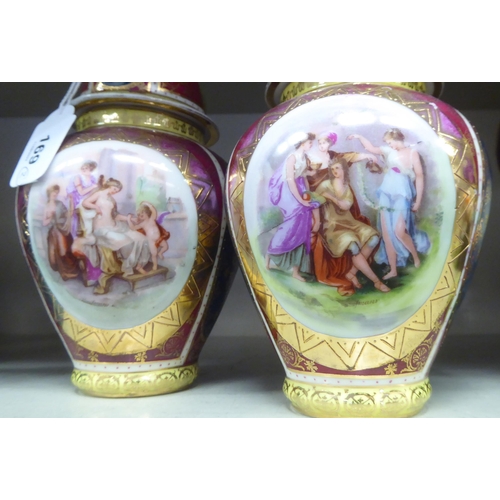 169 - A pair of early 20thC Vienna porcelain vases and covers, decorated with gilded cartouches, on a mult... 