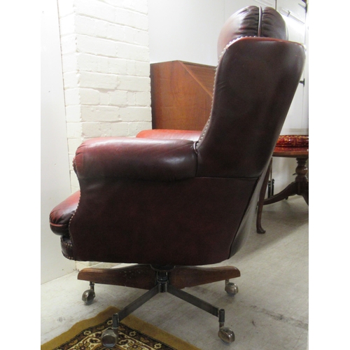 176 - A 20thC desk chair, stud upholstered in ox blood coloured hide, on a swivel base, splayed legs and c... 