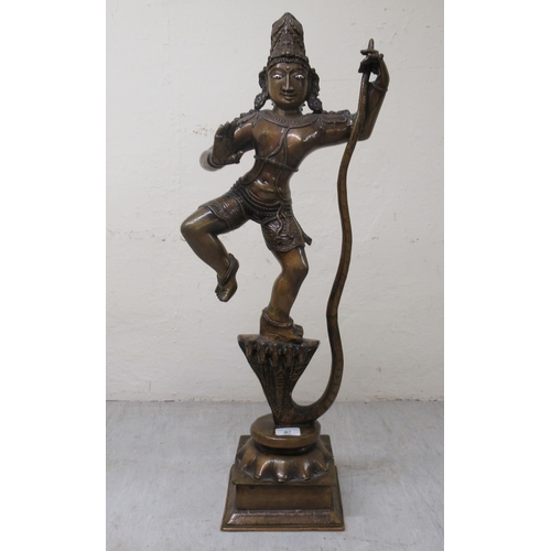 194 - A 20thC patinated bronze figure, Krishna, wearing ceremonial costumes, dancing with, and on, the hea... 