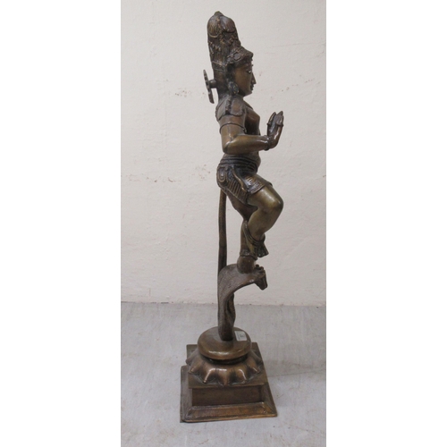 194 - A 20thC patinated bronze figure, Krishna, wearing ceremonial costumes, dancing with, and on, the hea... 