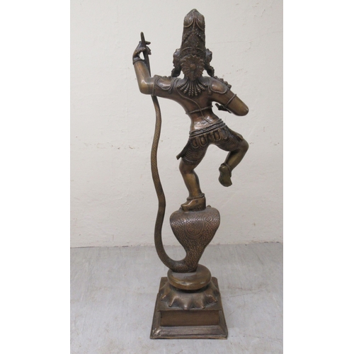 194 - A 20thC patinated bronze figure, Krishna, wearing ceremonial costumes, dancing with, and on, the hea... 