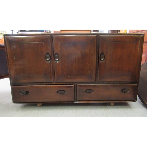 219 - An Ercol dark stained elm sideboard with three doors, over two inline drawers, on a plinth and caste... 